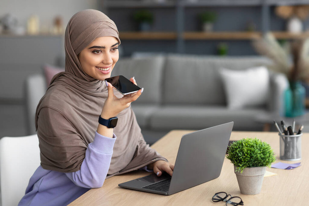Muslim woman using voice search assistant on smart phone - Fotó, kép