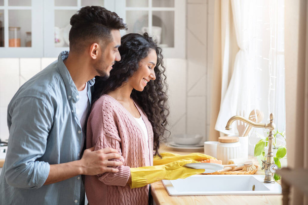 Портрет счастливых молодых ближневосточных супругов, моющих посуду после обеда на кухне - Фото, изображение