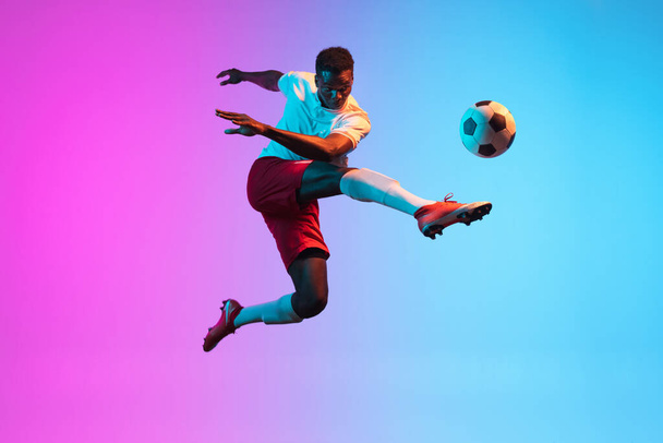 One African man, professional soccer football player training isolated on gradient blue pink background in neon light. - Fotoğraf, Görsel