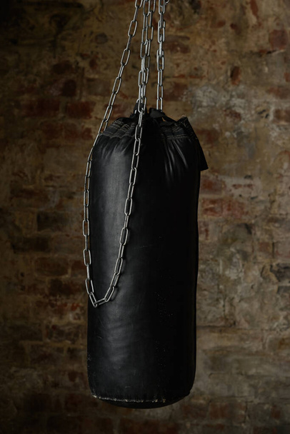 black punching bag on chains on the background of an old wall - Фото, изображение
