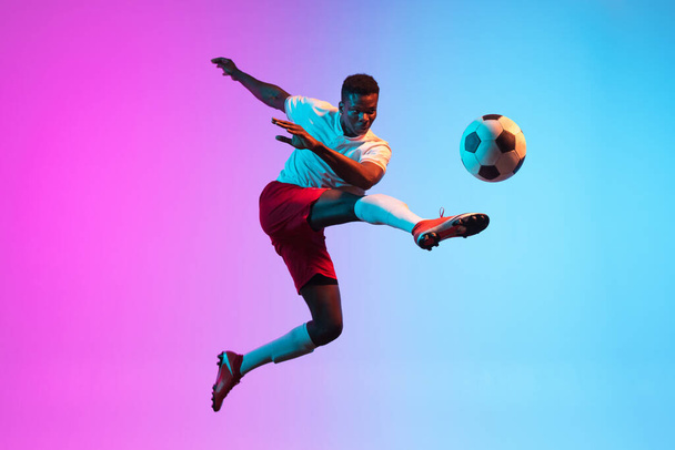 One African man, professional soccer football player training isolated on gradient blue pink background in neon light. - Фото, изображение