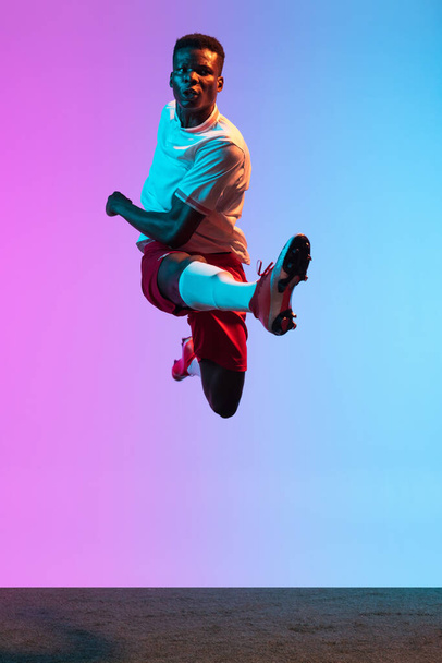 One African man, professional soccer football player training isolated on gradient blue pink background in neon light. Front view - Fotoğraf, Görsel