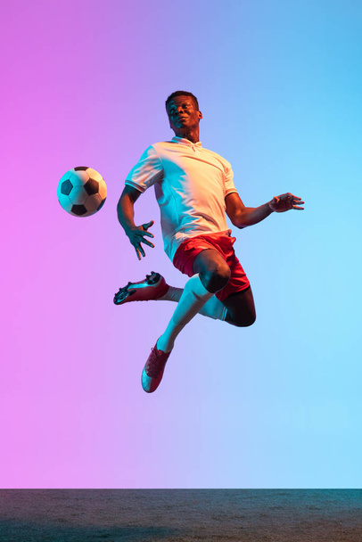 Portrait of African professional football player standing isolated on gradient blue pink background in neon light. Back view - Photo, image