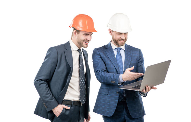 dos hombres de negocios socios en traje y casco de seguridad que trabajan en el ordenador portátil en línea aislado en blanco, socios de negocios. - Foto, imagen