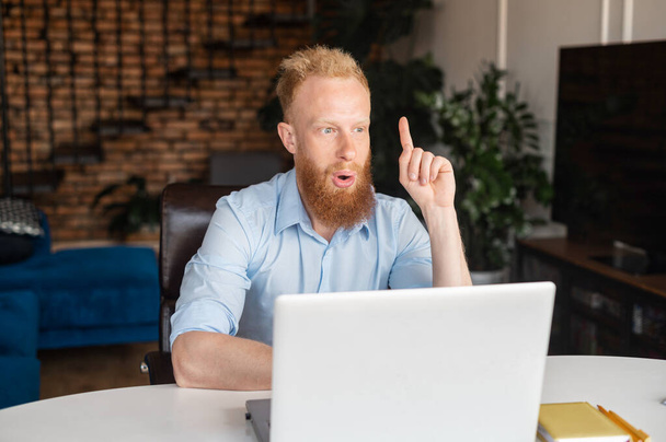 Redhead bearded man points index finger up with amazed face - Photo, Image