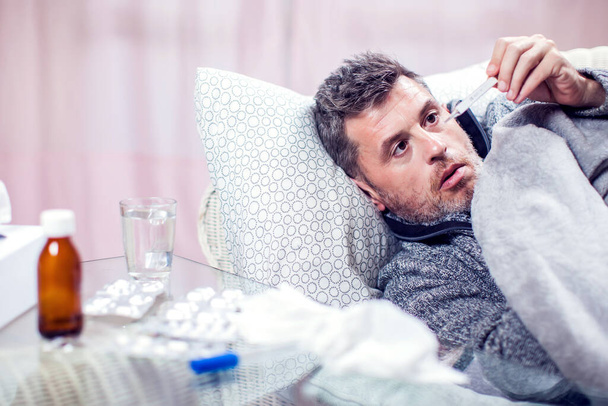 Ο άντρας με το μπλε κασκόλ κόλλησε γρίπη και θερμοκρασία μέτρησης. Άνθρωποι, υγειονομική περίθαλψη και ιατρική έννοια - Φωτογραφία, εικόνα