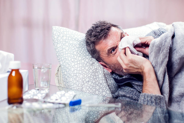 Man with blue scarf got the flu and blowing nose into napkin. People, healthcare and medicine concept - Photo, Image