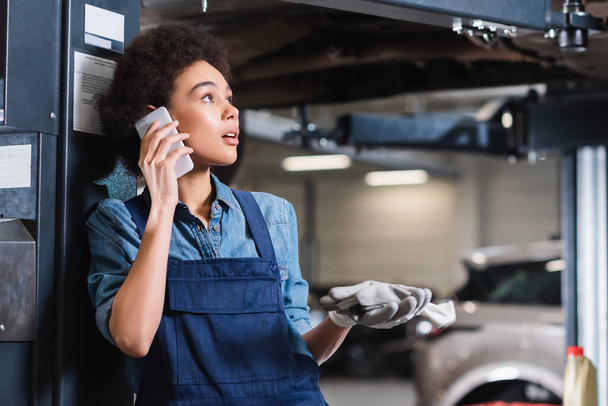 Huolestunut nuori afrikkalainen amerikkalainen mekaanikko puhuu kännykkään autotallissa - Valokuva, kuva