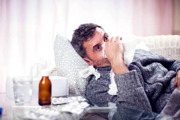 El hombre con bufanda azul tiene gripe y se sonó la nariz en la servilleta. Concepto de personas, salud y medicina - Foto, Imagen