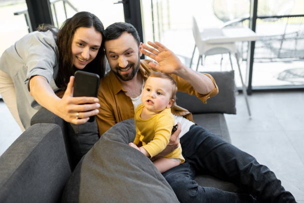 Щаслива сім'я з однорічною дитиною, яка має відеодзвінок по телефону
 - Фото, зображення