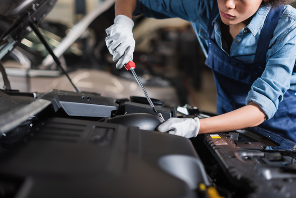 partial view of young african american mechanic holding screwdriver and fixing car motor in garage - 写真・画像