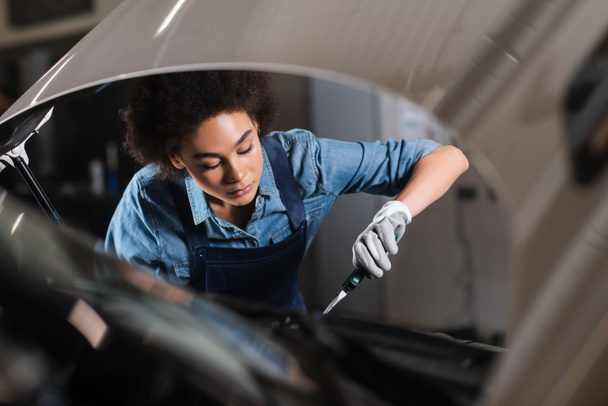 young african american mechanic holding pliers and working with motor of car in garage  - Photo, Image