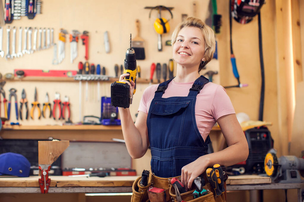 Молодая улыбающаяся женщина с короткими светлыми волосами, работающая с отвёрткой.  - Фото, изображение
