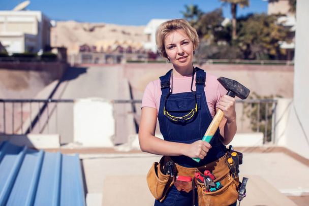 Young smiling handy woman with short blond hair working with hammer.  - 写真・画像