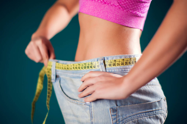 Frau trägt große Jeans mit Metermaß am Gürtel. Gewichtsverlust, Fitness und Ernährungskonzept - Foto, Bild