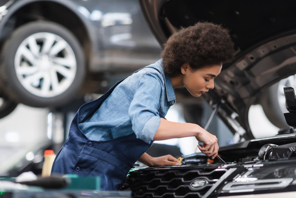 junger afrikanisch-amerikanischer Mechaniker hält Schraubenzieher und fixiert Automotor in Garage - Foto, Bild