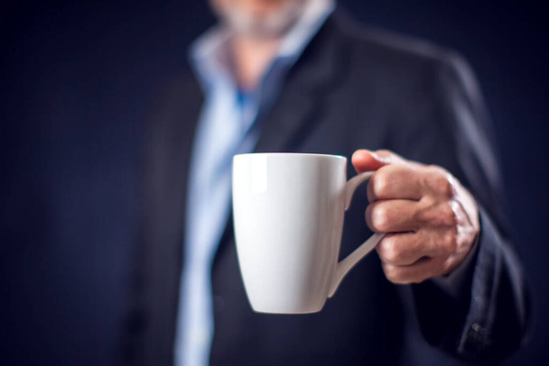 Businessman in suit holding cup of tea or coffee in hand in front of black background. Coffee break concept - Φωτογραφία, εικόνα