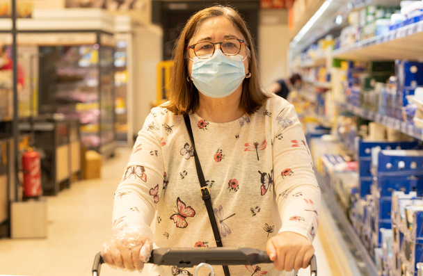 Ältere Frau kauft Lebensmittel im Lebensmittelgeschäft, trägt medizinische Maske. - Foto, Bild