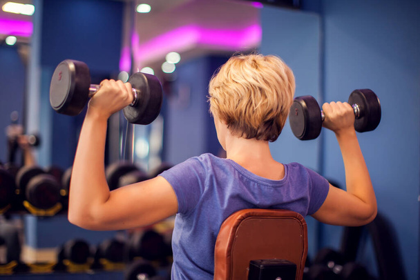 Woman in blue shirt with short hair training with dumbbells in the gym. People, fitness and health concept - Fotografie, Obrázek