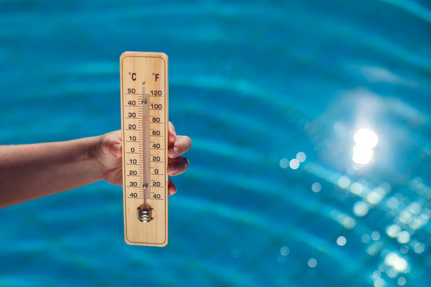 Woman holding thermometer on the blue pool background. Hot weather and summer concept - Foto, Imagen