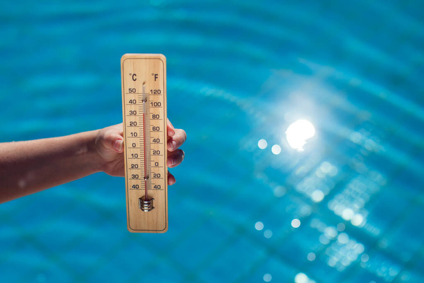 Woman holding thermometer on the blue pool background. Hot weather and summer concept - Fotografie, Obrázek