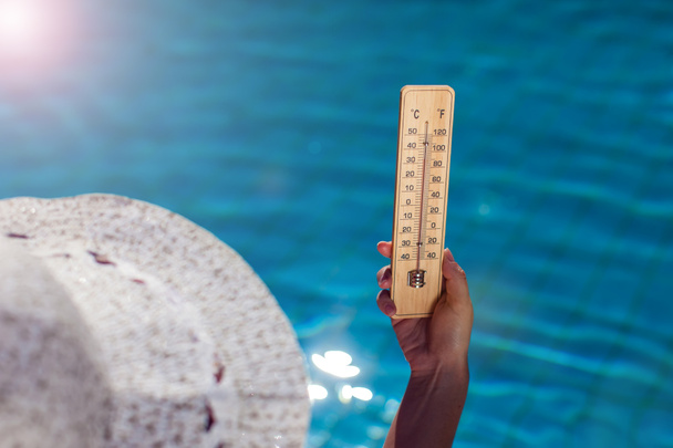 Woman holding thermometer on the blue pool background. Hot weather and summer concept - Valokuva, kuva
