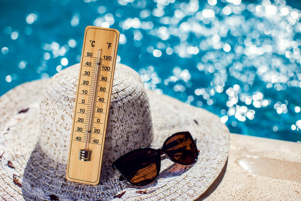 Woman's hat, thermometer and sunglasses lying beside the pool. Hot weather, summer and holiday concept - Photo, image