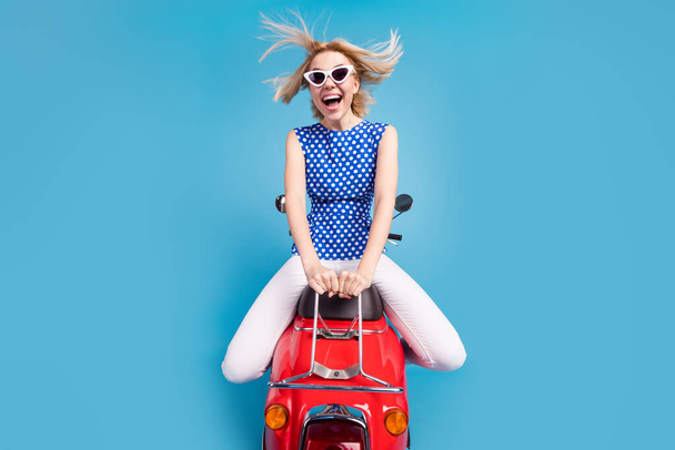 Foto von jungen aufgeregten Mädchen glücklich positives Lächeln Fahrt Motorrad Geschwindigkeit fliegen Schlag Haare isoliert über blauer Farbe Hintergrund - Foto, Bild