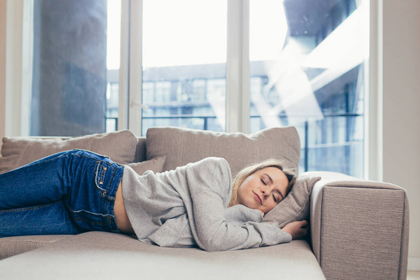 Young woman sleep resting at home on couch after a hard day's work. Relax calm and rest. On a soft cozy comfortable sofa. Comfort safety. Female with closed eyes feels comfortable and safe in warmth - Foto, afbeelding