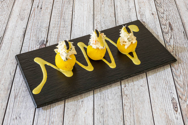 Sanduíches de causa de Lima em um prato de ardósia adornado com vestígios de molho amarelo em uma mesa preta - Foto, Imagem