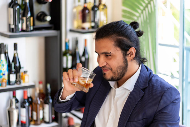 Mladý latinoameričan sedí na domácí skříňce a pije whisky. Nový normální. - Fotografie, Obrázek