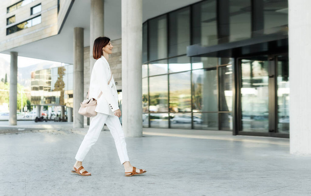 Schöne Millennial stilvolle Hipsterfrau mittleren Alters, die draußen in weißen Kleidern spaziert. Erfolg im Geschäftsviertel, Kopierraum - Foto, Bild