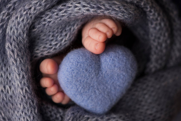 Zwei niedliche winzige Babyfüße, eingewickelt in eine blau-grüne Aqua-Strickdecke. Und ein gestricktes Herz aus Wollfäden. - Foto, Bild