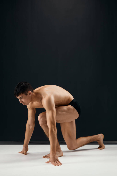 Bodybuilder in schwarzen Shorts steht kniend vor dunklem Hintergrund - Foto, Bild