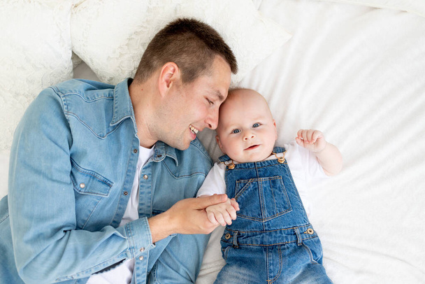 ευτυχισμένος πατέρας με το μωρό γιο ξαπλωμένος στο κρεβάτι και αγκαλιάζει διασκεδάζοντας, την έννοια της ημέρας του πατέρα ή την πατρότητα - Φωτογραφία, εικόνα