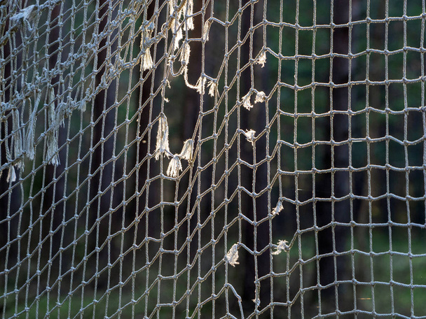 Futbol gollerinin eski yırtık pırtık ağı güneş tarafından aydınlatılıyor. İp ağ arkaplanı. - Fotoğraf, Görsel