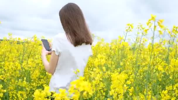 Mujer joven en una camiseta blanca entre un campo de flores amarillas - Metraje, vídeo