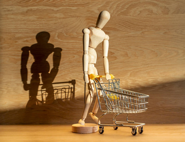 Burden of shopping concept. Wooden man bent and leaning over shop cart in beautiful day light - Фото, изображение
