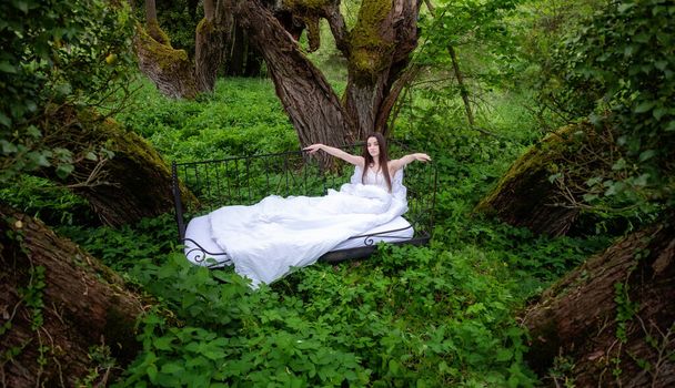 приваблива, молода, сексуальна жінка на відкритому повітрі в ліжку, брюнетка, в білому нічному одязі, в природі чарівна казка ліс
 - Фото, зображення