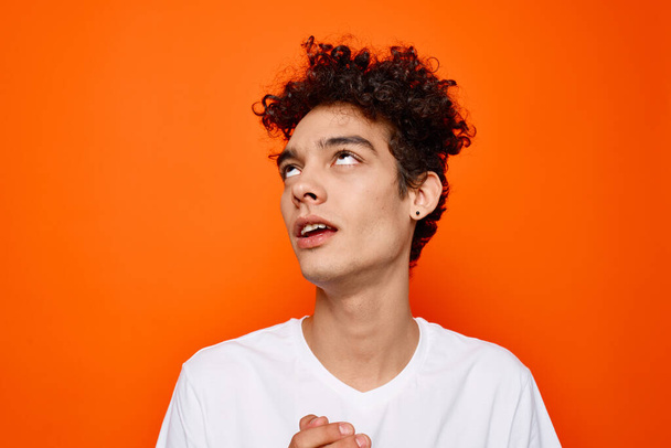 young guy in white t-shirt curly hair smile orange background - Foto, afbeelding
