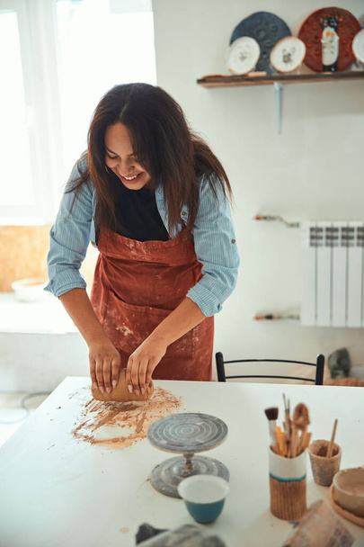 Mujer alegre en delantal trabajando en taller de cerámica - Foto, imagen