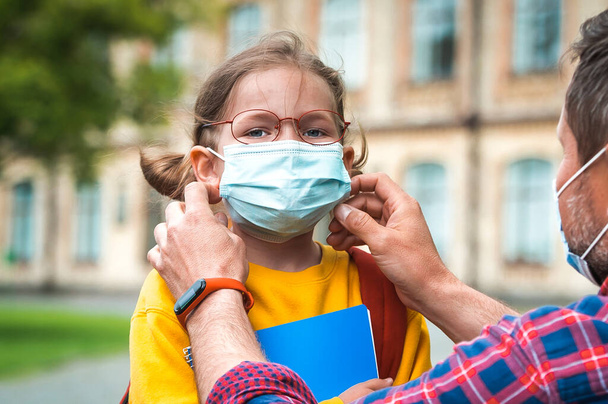Father putting on face mask to prevent coronavirus covid-19 and viral infections. Dad helping little girl with protective mask. Teacher on coronavirus pandemic. Dad and daughter going back to school. - Photo, Image