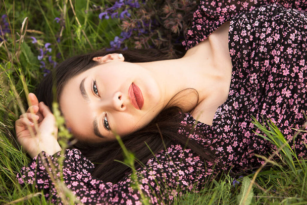 Portret młodej pięknej dziewczyny leżącej wśród dzikich kwiatów i trawy w słoneczny dzień na łące. - Zdjęcie, obraz