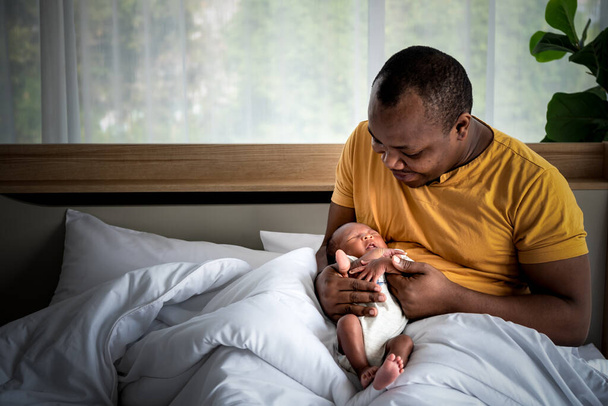 Un padre africano, mirando y tomándose de la mano a un bebé recién nacido de 12 días con cuidado y felicidad, a la relación de la familia africana y el concepto de recién nacido. - Foto, Imagen
