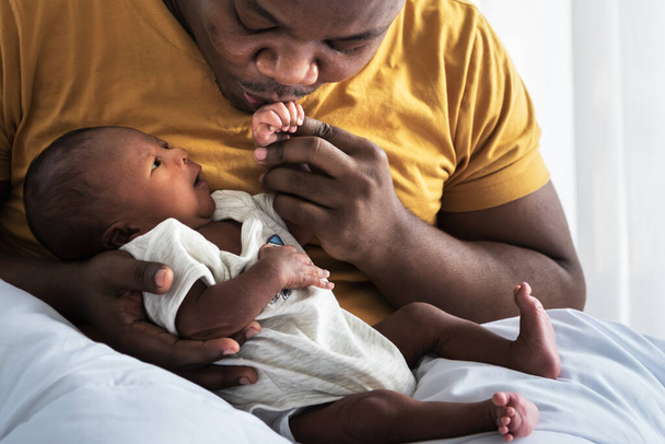 Um pai afro-americano beijando a mão, seu filho recém-nascido de 12 dias deitado na cama em um quarto branco, com feliz, conceito para a família afro-americana e recém-nascido - Foto, Imagem