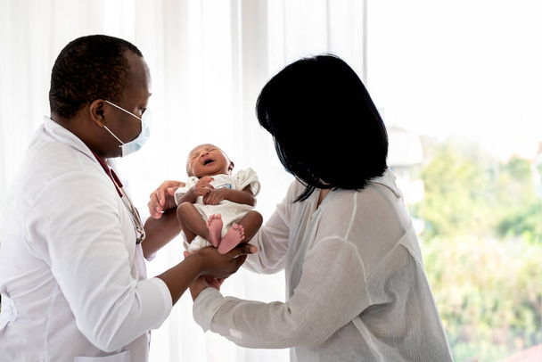 Imágenes blandas enterradas de la Madre sostiene a un bebé de 12 días de edad, hijo recién nacido, enviado a un médico africano que lleva una máscara quirúrgica, para un chequeo de salud, para el bebé y el concepto de atención médica. - Foto, Imagen