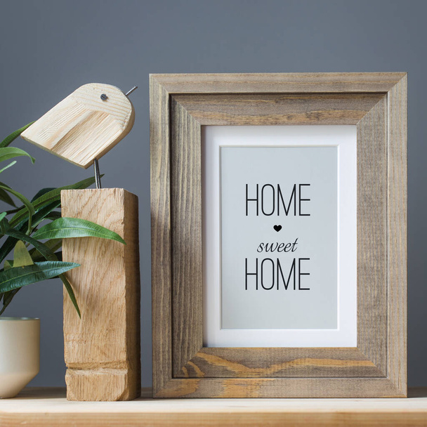 photo frame with text home sweet home, wooden craft toy and artificial flower in pot on gray background. - Photo, image