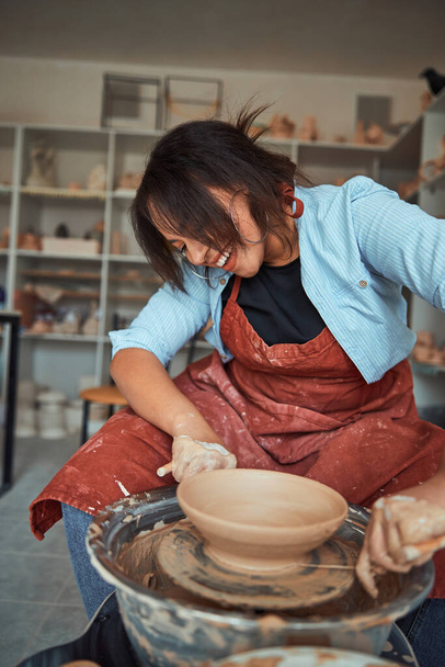陶芸教室でクレイボウルを作る陽気な若い女性 - 写真・画像