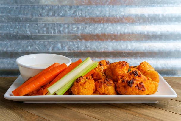 Vegetarian cauliflower buffalo wings served with blue cheese dipping sauce and sliced carrots and celery - Photo, Image
