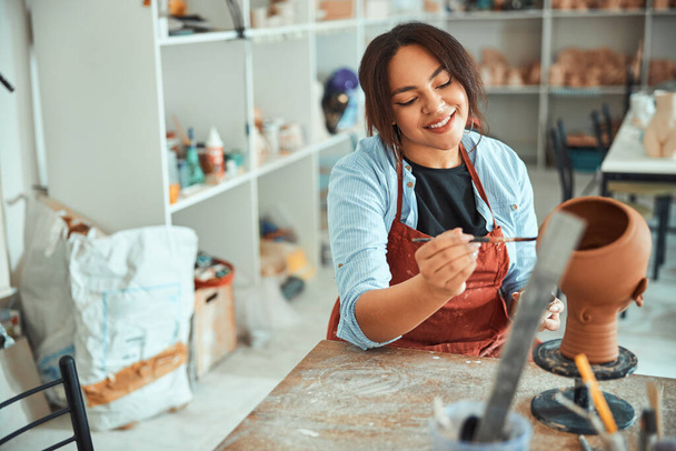 Cheerful young woman painting pottery in workshop - Photo, Image